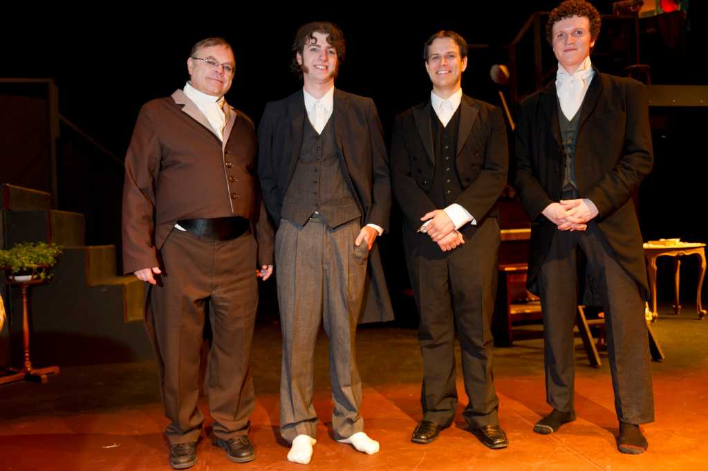 Four men dressed in 19th century costume stand in a line.